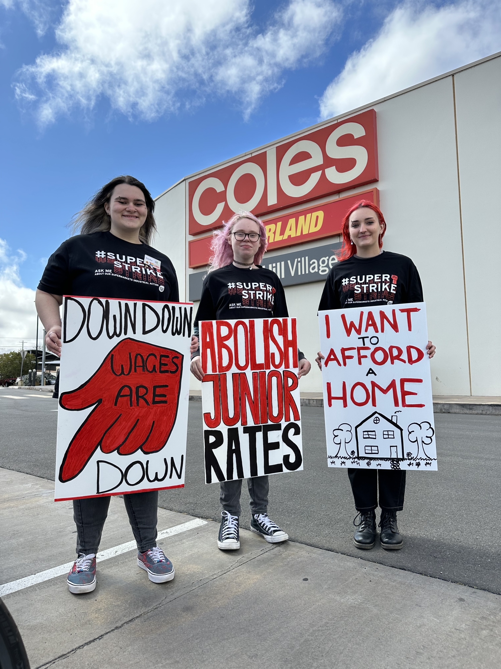 Three young supermarket workers and union members on strike, with signs that say "Abolish junior rates" and "I want to afford a home".